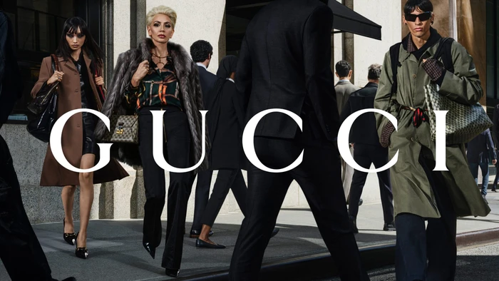 Models in fashionable attire walking along a bustling city sidewalk with the Gucci logo overlaid prominently.