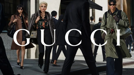 Models in fashionable attire walking along a bustling city sidewalk with the Gucci logo overlaid prominently.