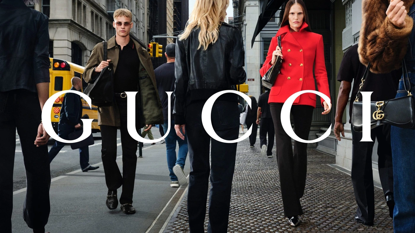 Models walking on a city sidewalk in New York City with a yellow school bus and buildings in the background for Gucci Fall 2026