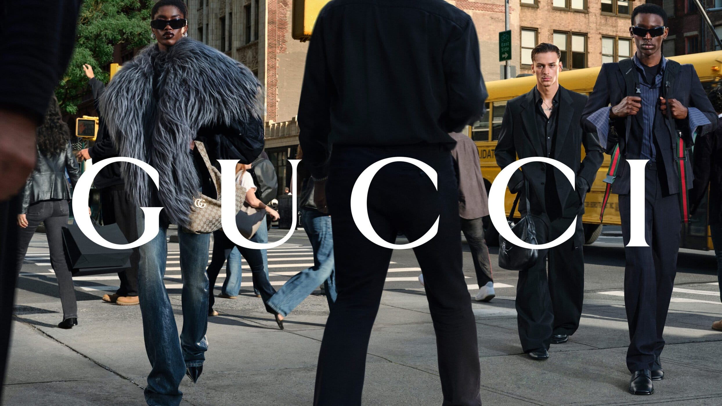 Group of models walking on a New York City street with a yellow bus in the background wearing Gucci