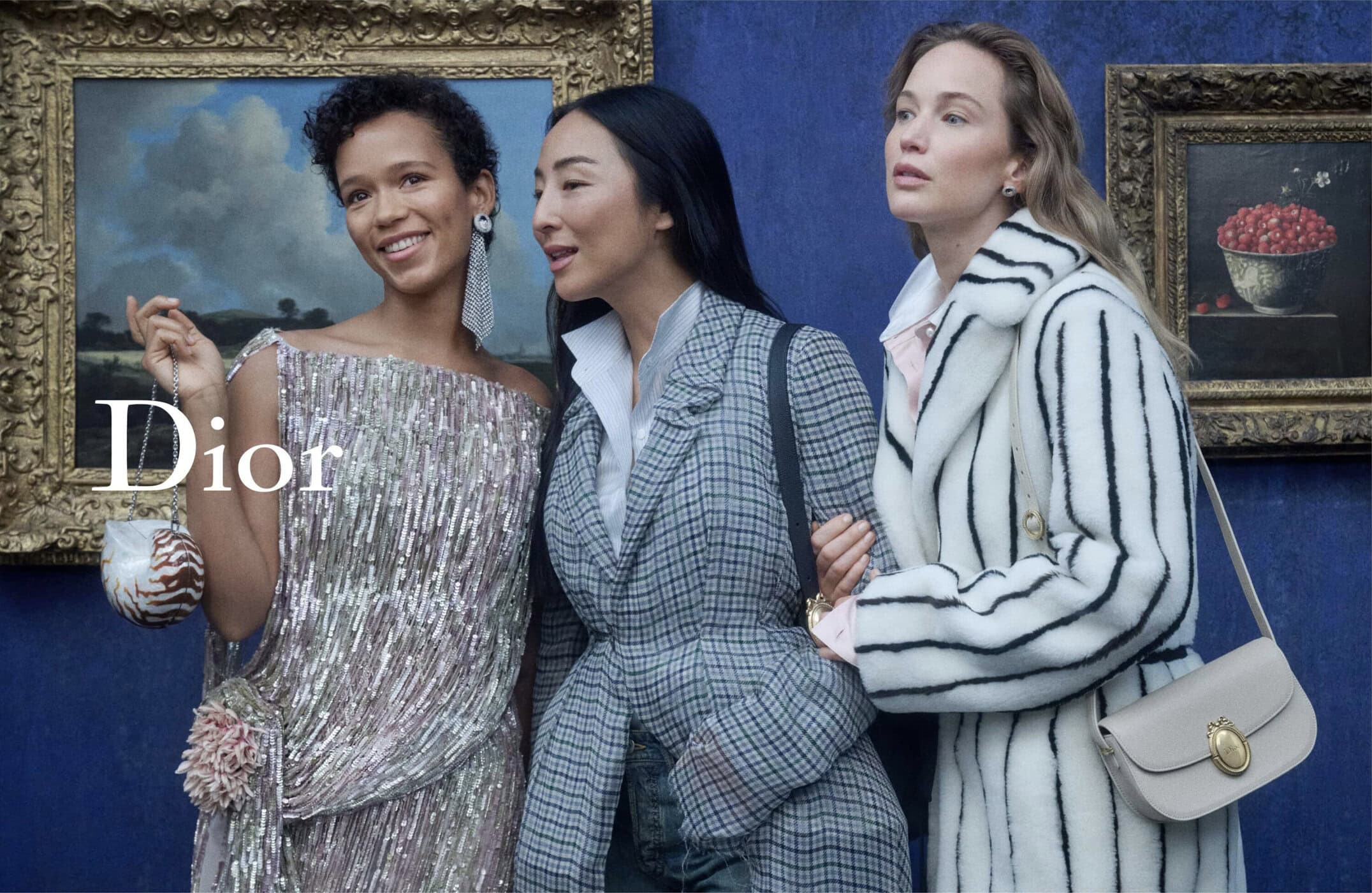 Three models posing in front of framed classical paintings against a textured blue wall for a Dior campaign