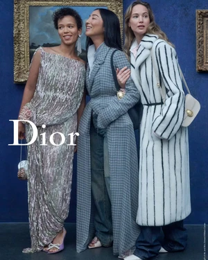 Three models in designer apparel pose against a deep blue wall with framed artwork for the Dior Cruise 2027 campaign.