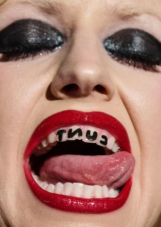 Close-up shot of a woman's face with red lipstick and heavy black eye makeup, sticking out her tongue with text on her teeth.