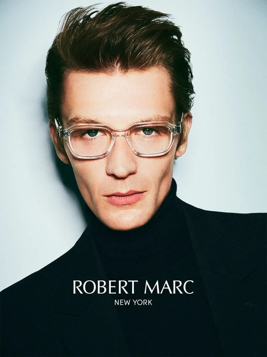 Close-up portrait of a male model wearing clear frame glasses and a black turtleneck against a light background