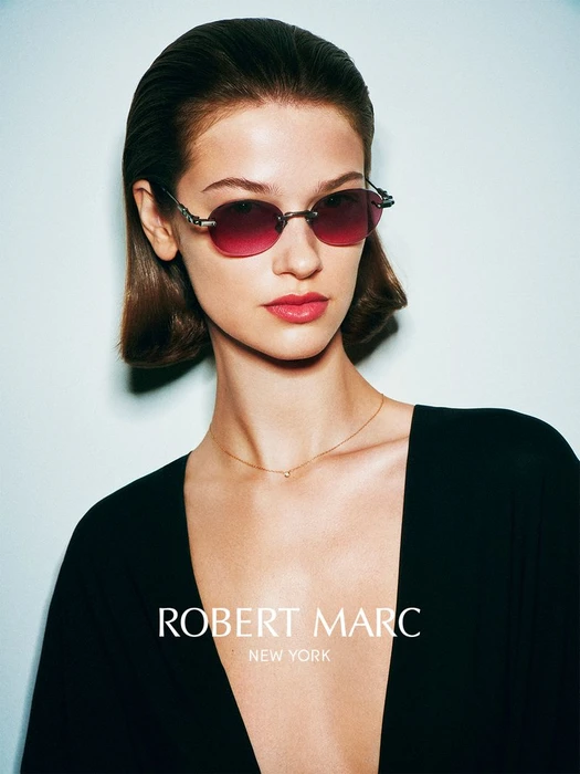 Model wearing dark rimless sunglasses with tinted lenses and a black V-neck top against a pale background