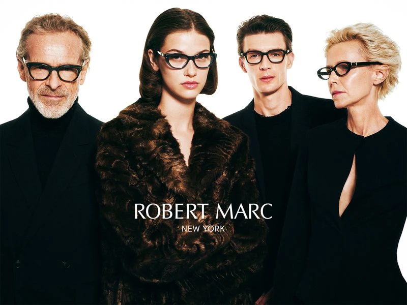 Four models wearing black outfits and eyeglasses pose against a white background with Robert Marc New York branding.