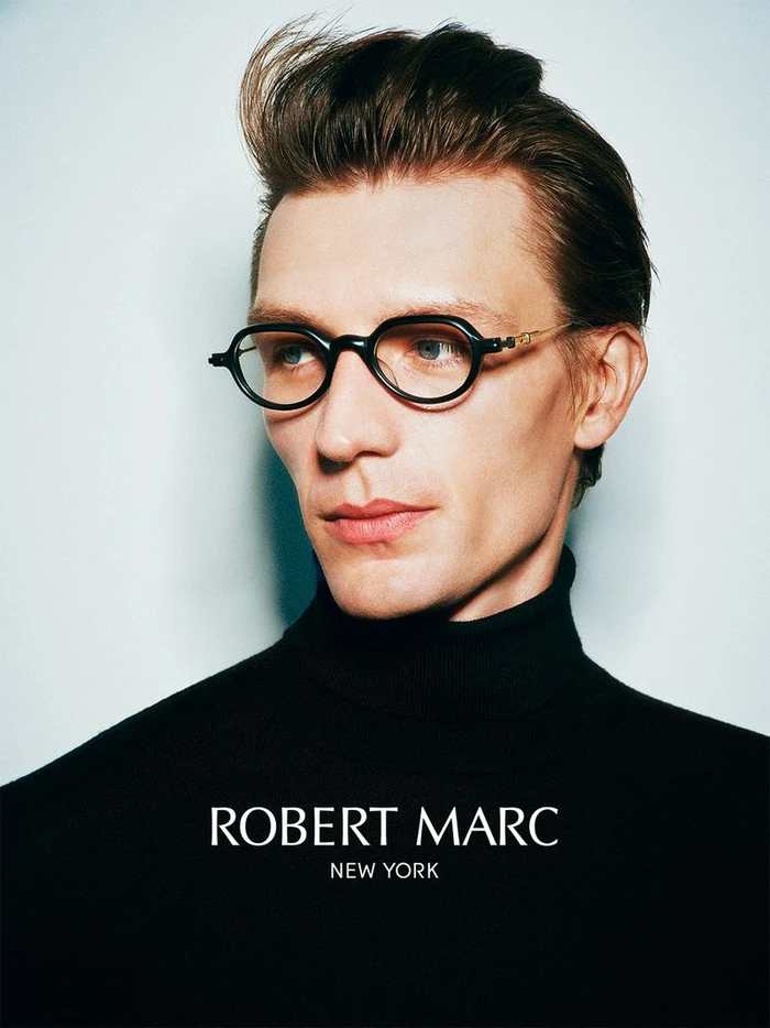 Man wearing dark eyeglasses and a black turtleneck sweater against a light background with overlaid white text.