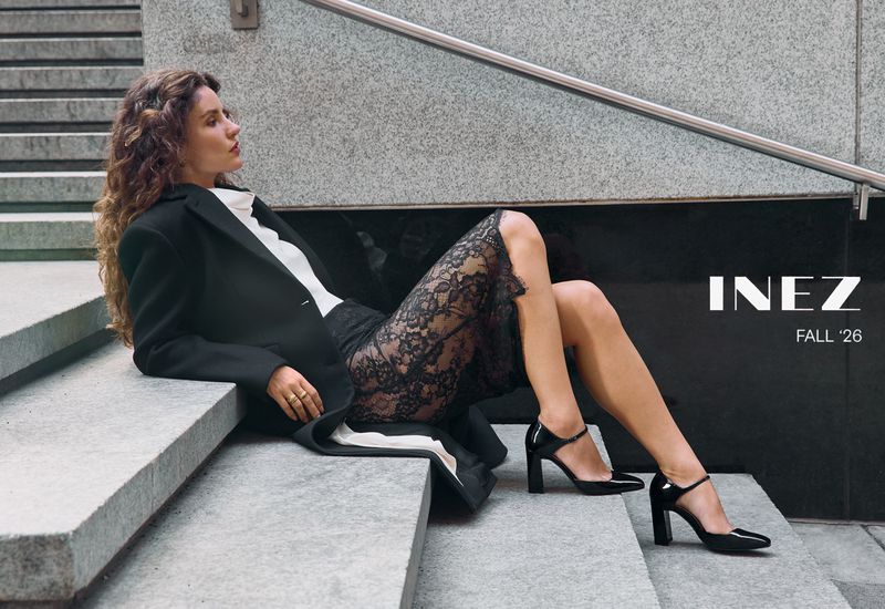 Woman in black coat and lace skirt seated on stone steps wearing heels for Inez Fall 2026