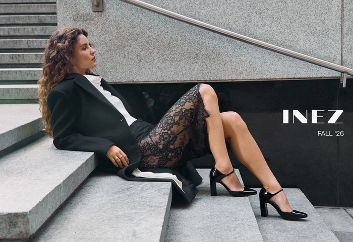 Woman in black coat and lace skirt seated on stone steps wearing heels for Inez Fall 2026