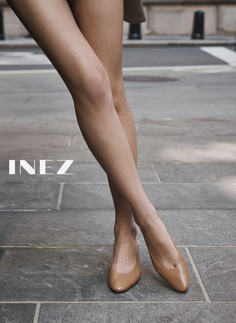 Close-up of a model standing on a stone sidewalk wearing tan leather flats for Inez Fall 2026 campaign.