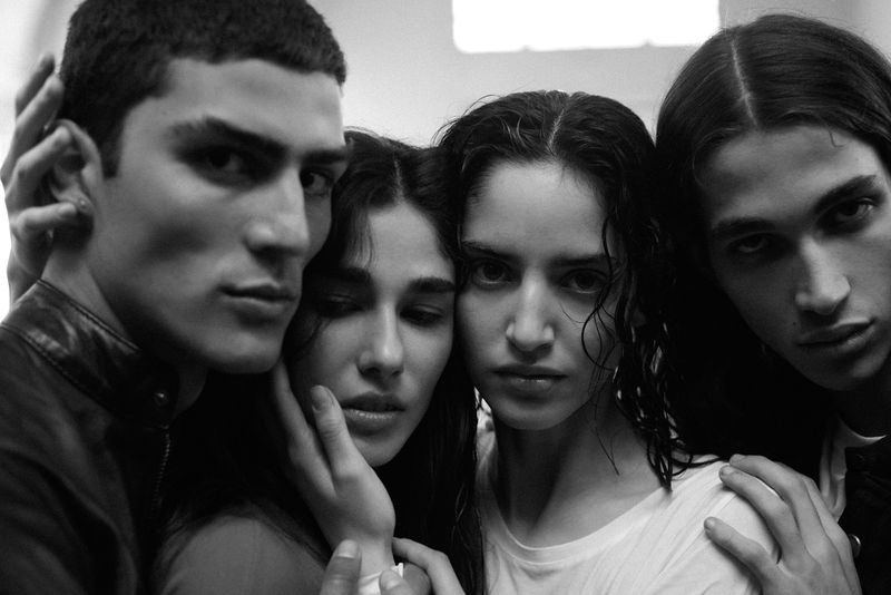 Close-up black and white portrait of four models posed closely together with hands gently touching faces.
