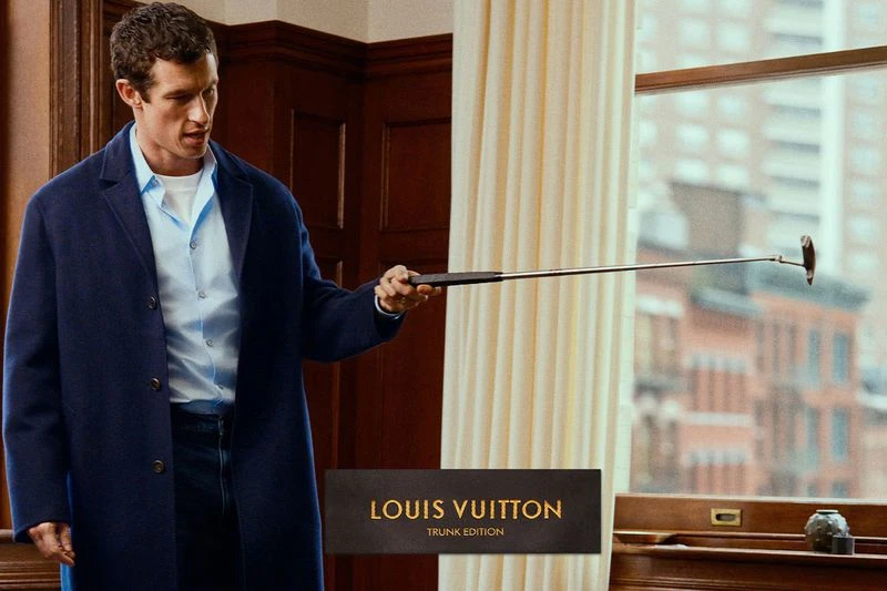 Callum Turner holding a golf putter wearing a blue coat and light blue shirt indoors for Louis Vuitton