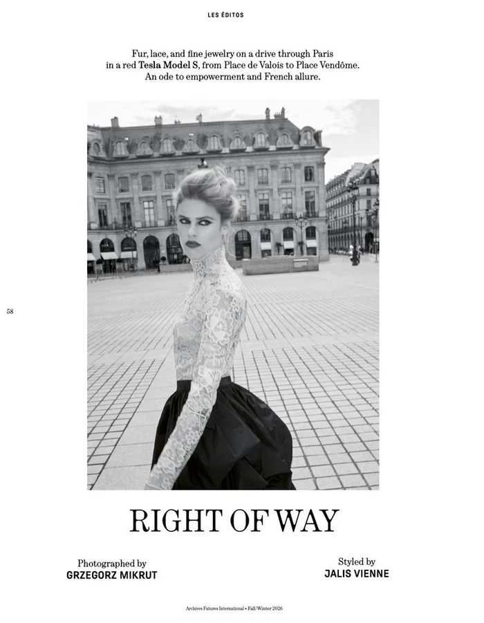 Model wearing a lace top and dark skirt standing in a cobblestone public square with classic European buildings