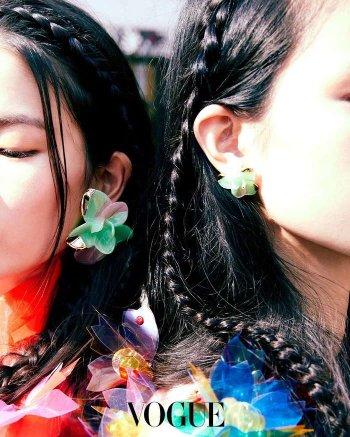 Close-up of two models with braided hair wearing translucent floral earrings and colorful accessories for Vogue Korea.