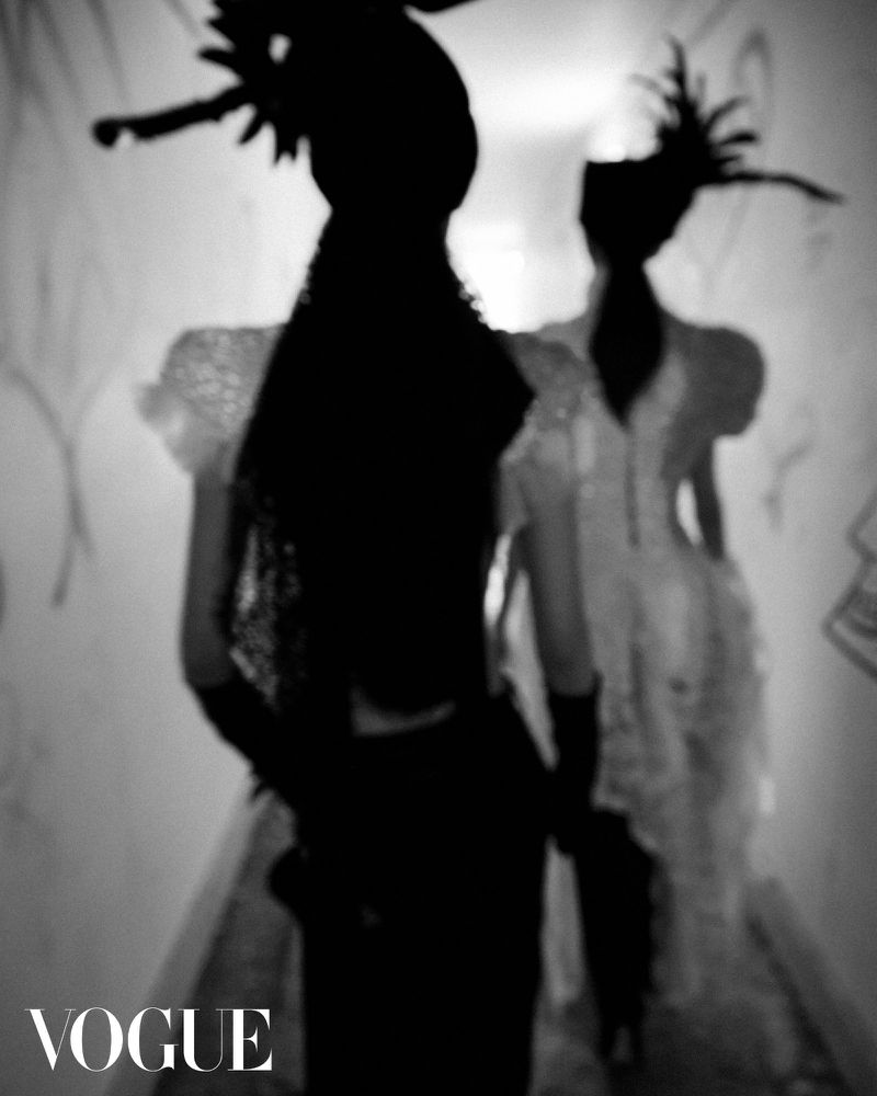 Two figures in dark silhouette wearing feathered headpieces walking down a corridor for Vogue Korea editorial