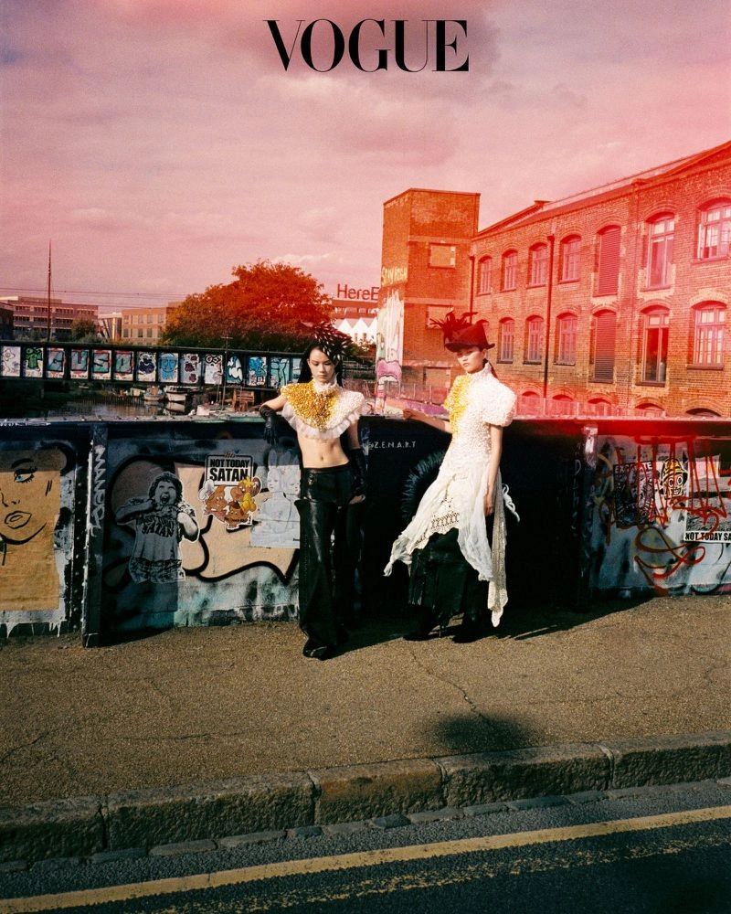 Two models in avant-garde outfits posing near a graffiti-covered wall under a reddish sky for a Vogue Korea editorial.