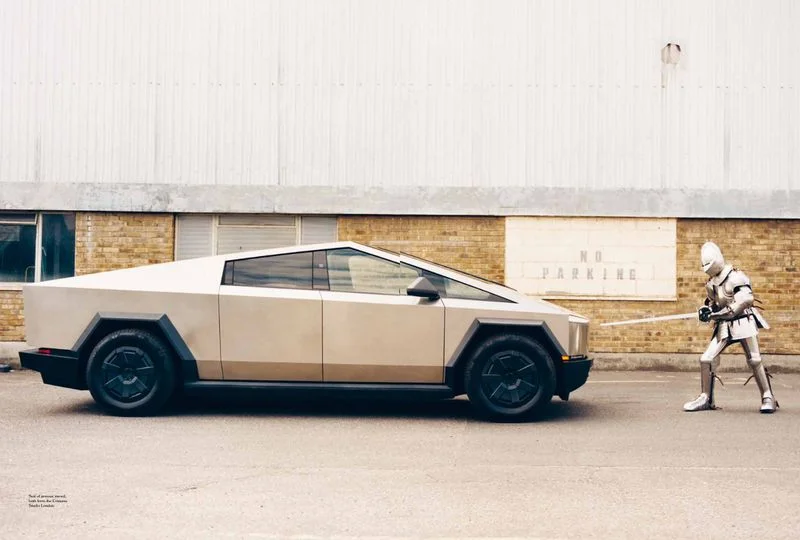 Silver electric pickup truck parked outdoors next to a person in full medieval metal plate armor holding a sword