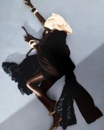 Model Achol Kuir lying on a light grey studio floor wearing dark clothing and a cream headwrap