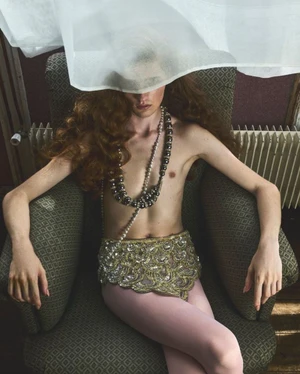 Model seated in an armchair with a sheer white fabric draped over their face for an editorial in Love Magazine Issue 27