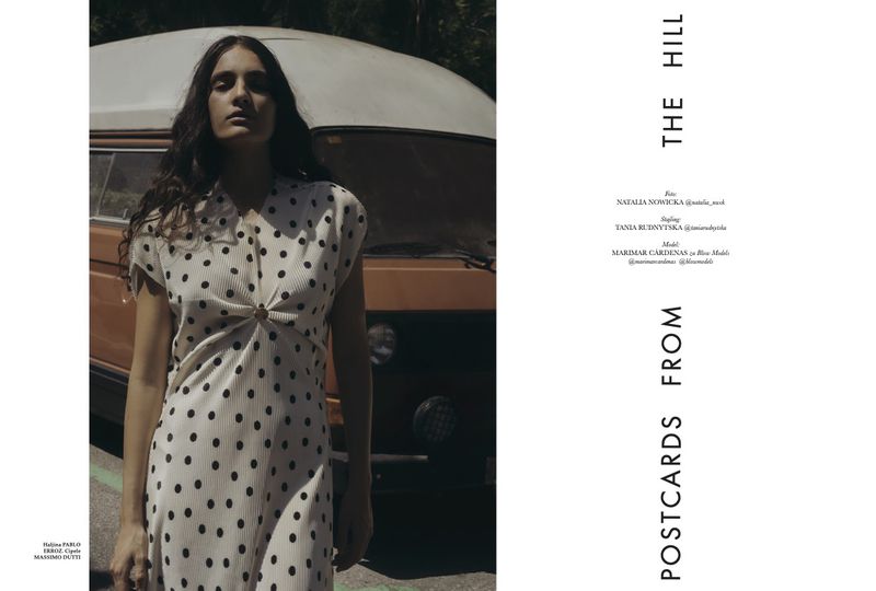 A woman poses in a polka dot dress next to a vintage van outdoors on a sunny day, creating a retro fashion editorial style image.