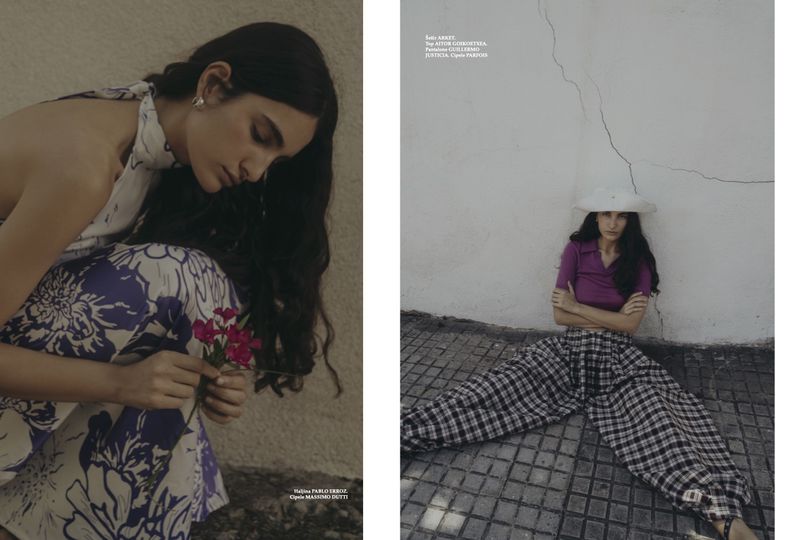 Two models pose outdoors; one wears a floral dress while holding pink flowers, the other wears a purple top and plaid pants.