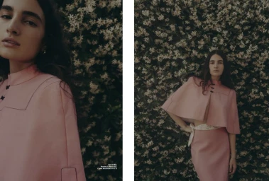 Model in a pink cropped cape and skirt posing against a dense flowering bush for Elle Serbia