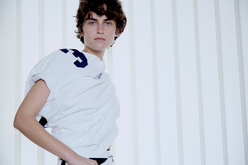 Model in white top with dark numbers posing against a vertical panel background
