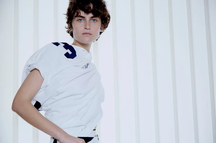 Model in white top with dark numbers posing against a vertical panel background