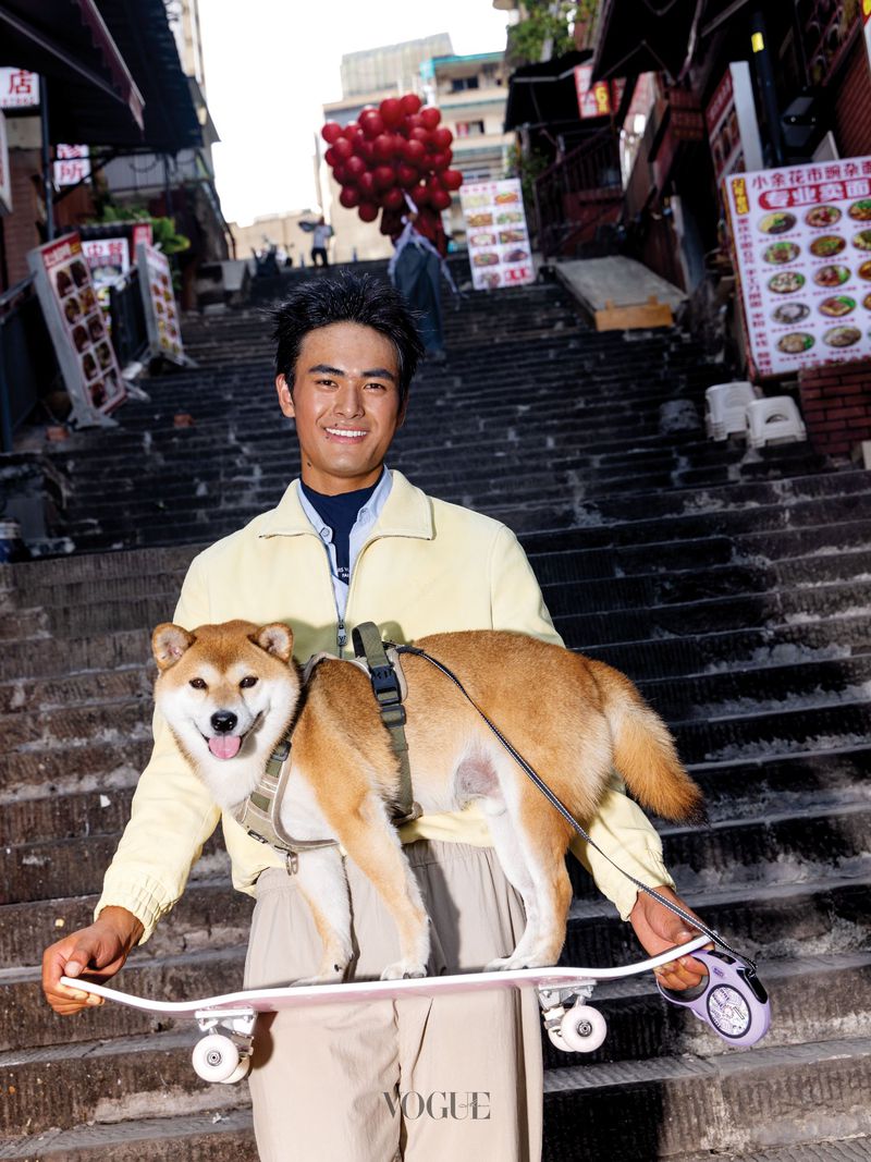 Man holding a skateboard with a Shiba Inu dog standing on it on outdoor stone steps in Chongqing for Vogue China Men