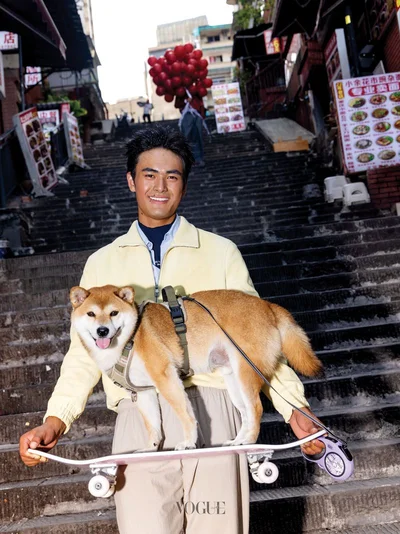 Man holding a skateboard with a Shiba Inu dog standing on it on outdoor stone steps in Chongqing for Vogue China Men