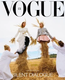Two female models styled as scarecrows in haystacks in a field, assisted by two figures in white coats.
