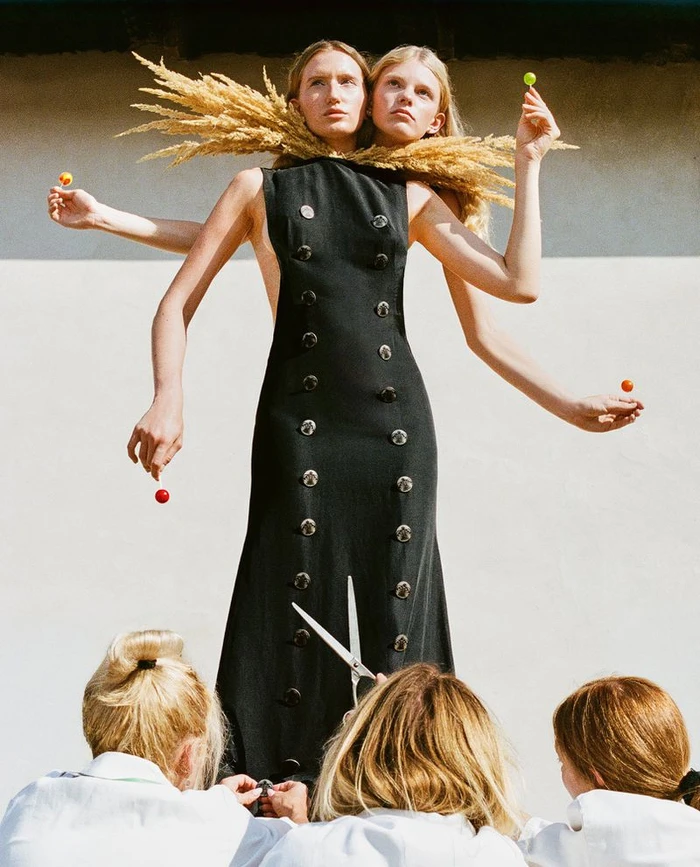 Model in a black double-breasted dress with multiple arms holding lollipops for Vogue Czechoslovakia by Michal Pudelka