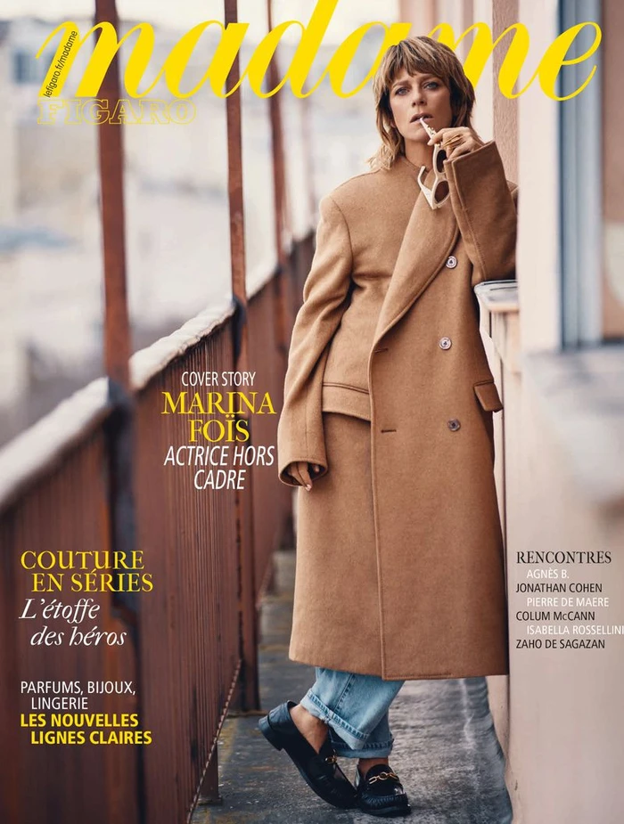 Marina Fois wearing a camel coat and blue jeans standing on a balcony for Madame Figaro magazine cover