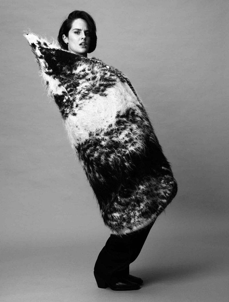 Noemie Merlant wrapped in a textured black and white patterned coat against a grey studio backdrop for Madame Figaro