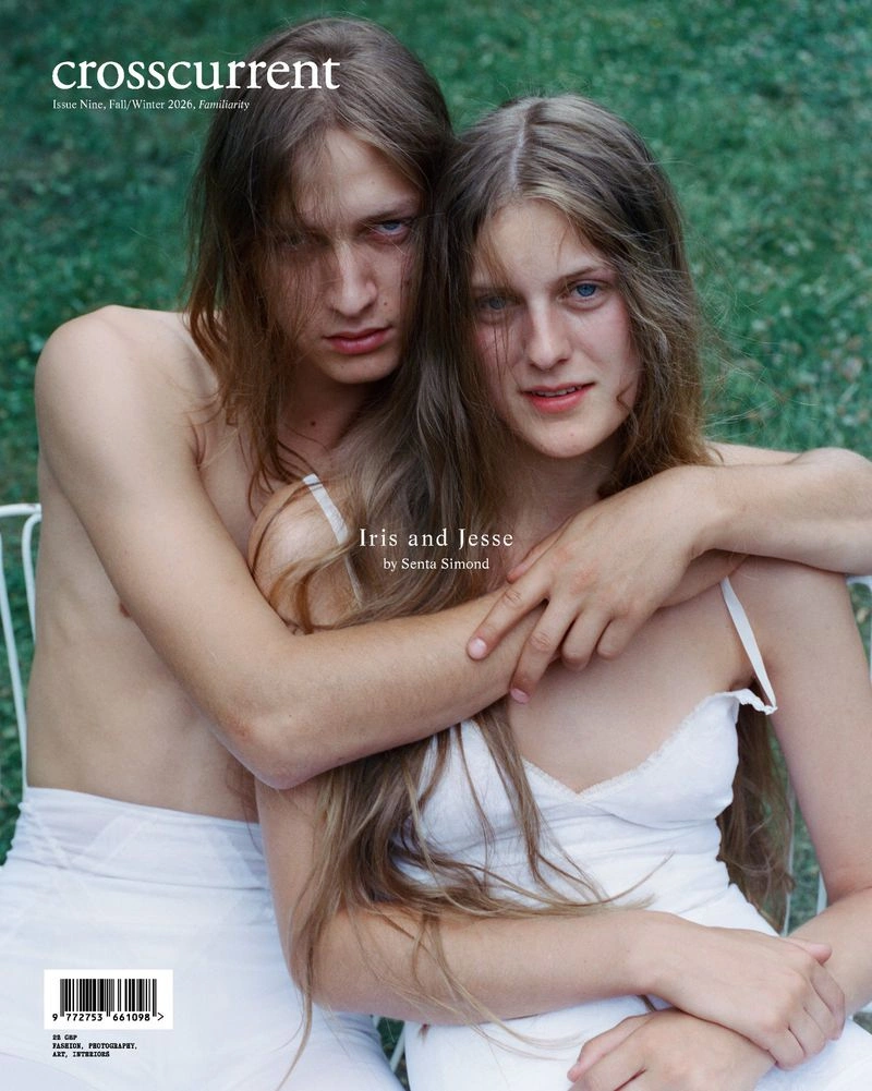 Two people with long brown hair embracing outdoors against a green grass background, wearing white apparel.