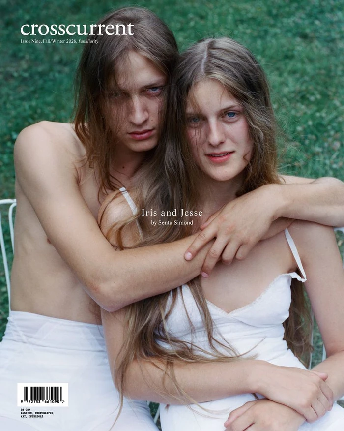 Two people with long brown hair embracing outdoors against a green grass background, wearing white apparel.