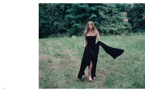 Model in a black strapless gown walking across a grassy field with trees in the background