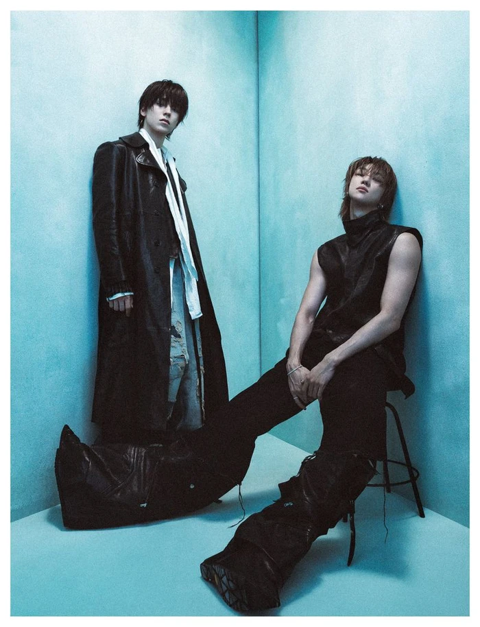 Two young male models in black leather attire posing against a blue corner wall for Numero Netherlands V8 project.