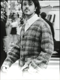 Black and white editorial portrait of actor Harry Richardson wearing a patterned cardigan on a city street.