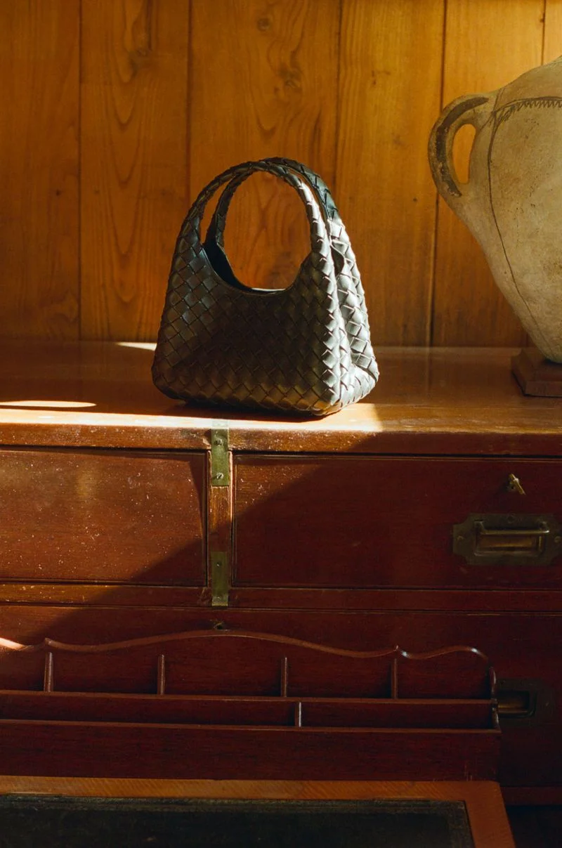 Black woven leather handbag resting on a polished wooden cabinet against wooden wall panels.