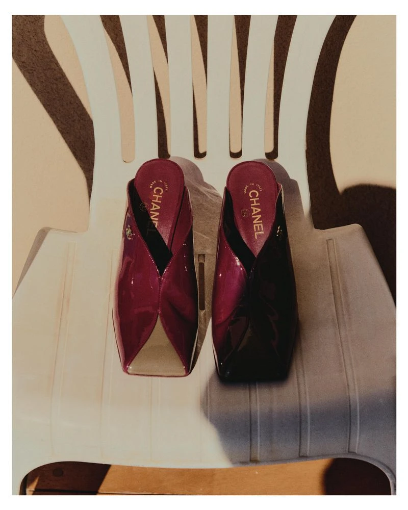 A pair of purple patent leather mules resting on a white plastic garden chair for Grazia Germany.