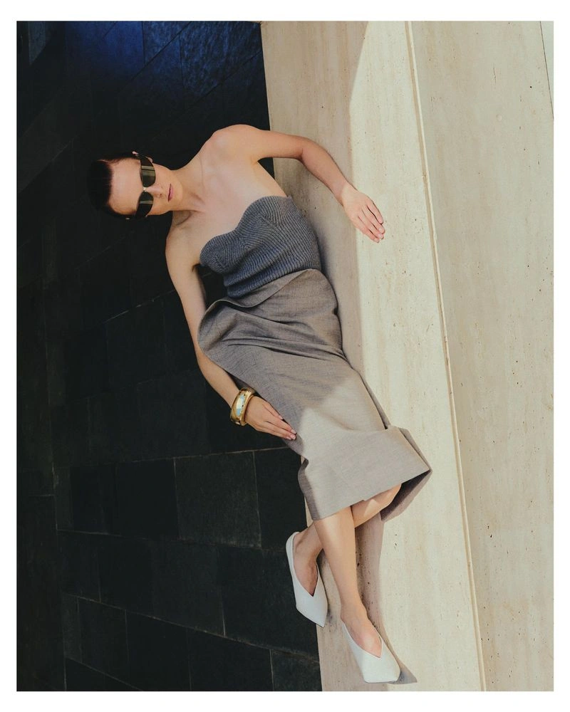 Model Dominika Pikula wearing a grey strapless top and skirt reclining against a structured stone wall for Grazia Germany.
