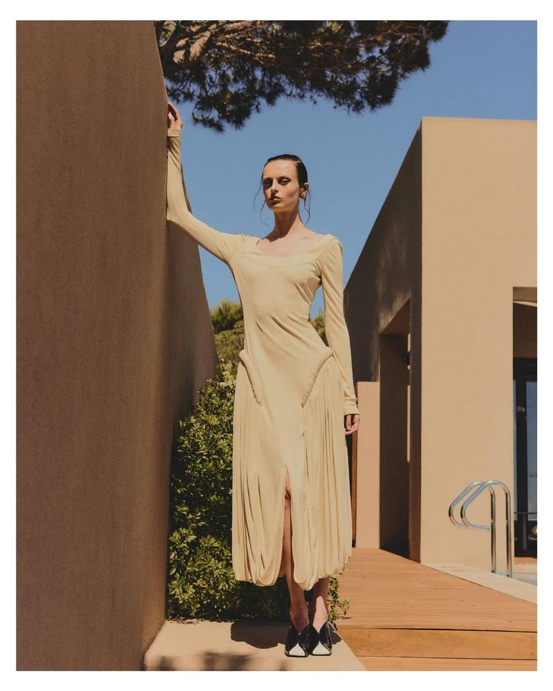 Model Dominika Pikula in a long beige dress leaning against a wall by a pool for Grazia Germany maximal minimal fashion editorial