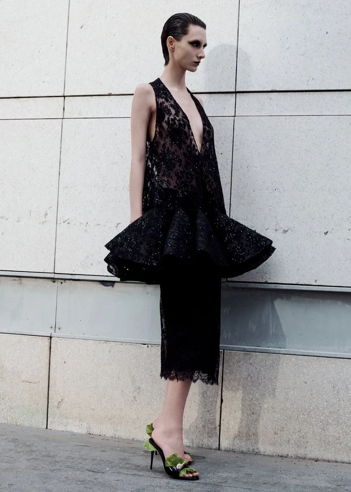Model in a black lace peplum dress standing against a tiled stone wall for Where in Paris project