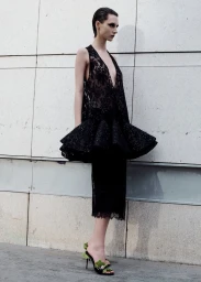 Model in a black lace peplum dress standing against a tiled stone wall for Where in Paris project