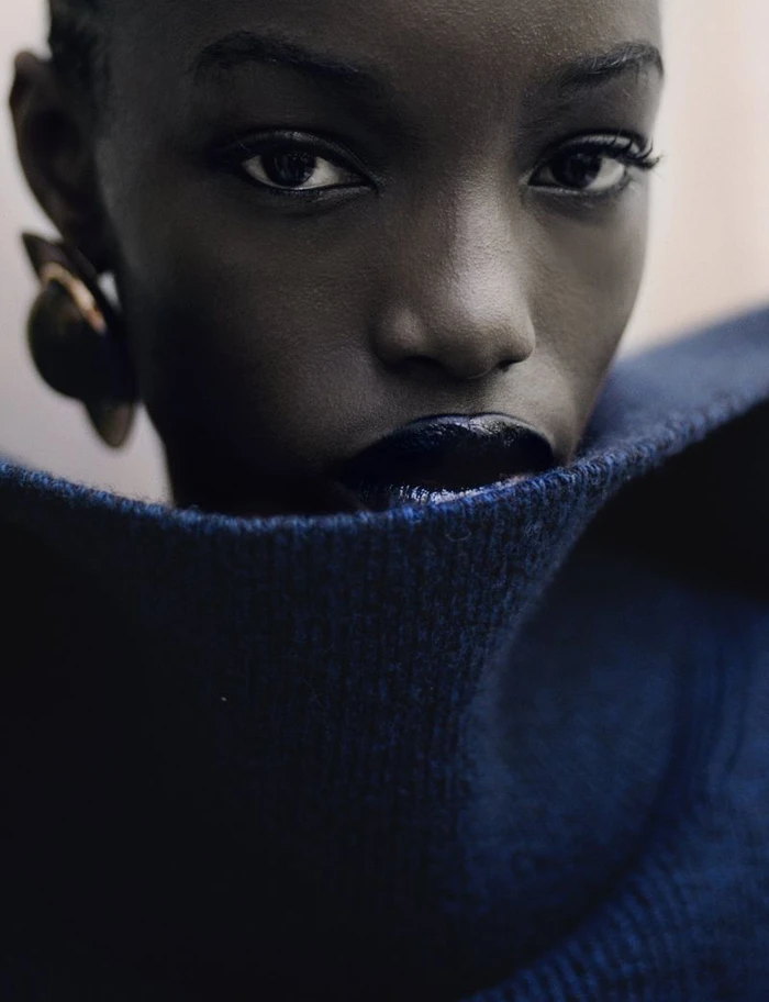 Close-up portrait of a Black woman in a blue turtleneck collar with dark lipstick and statement earrings
