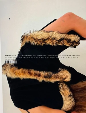 Model wearing dark garment with furry animal-print trim against a plain background