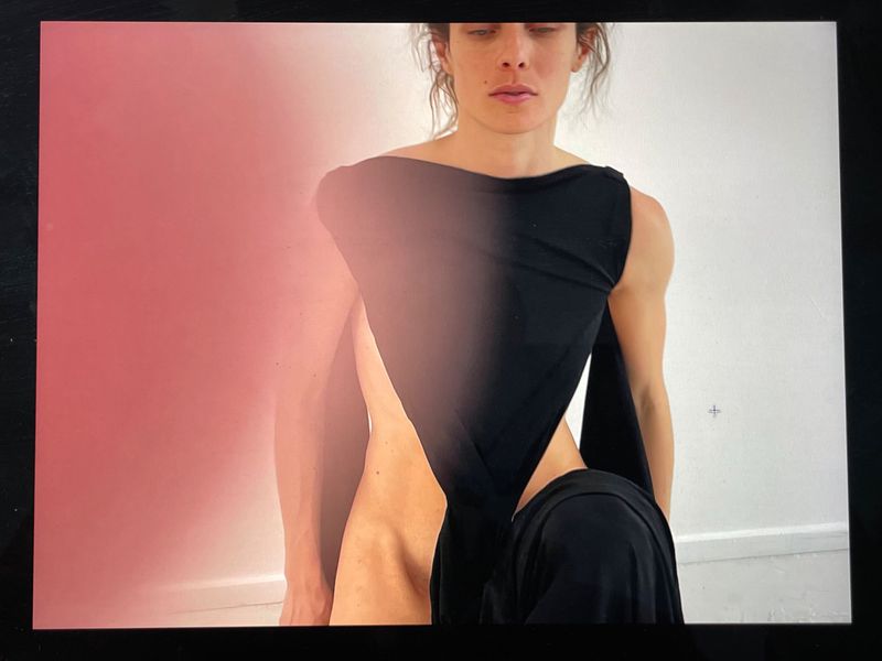 Model in a black asymmetrical garment against a white and pink gradient studio background