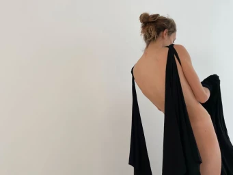 Model with hair in a bun wearing a draped black garment against a white background