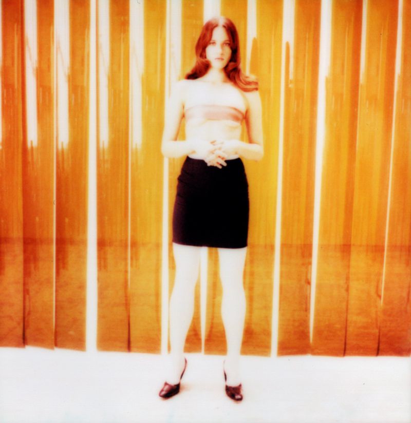 Model Julia Banas in a black miniskirt against a vertical orange striped backdrop for Middle Plane Magazine by Frank Lebon